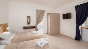 A hotel room with two beds, a wardrobe, a TV, and a window with curtains. - Island Guesthouse (Gzira)