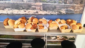 A variety of baked goods displayed in baskets on a table, with a cityscape view in the background. - Island Guesthouse (Gzira)