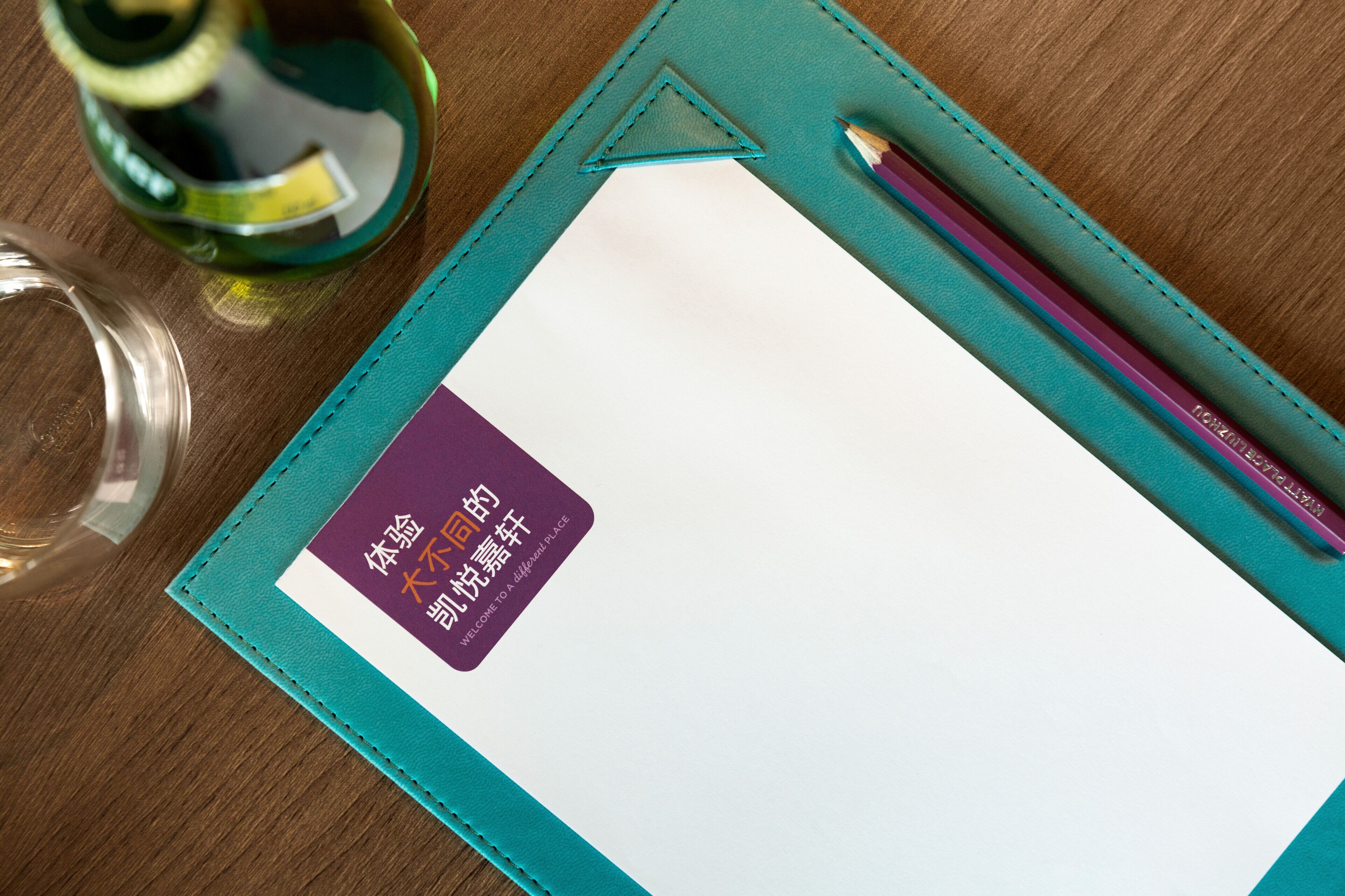 Un carnet avec une étiquette violette, un stylo et un verre d’eau sur une table en bois.