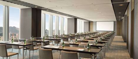 A conference room with rows of tables and chairs, large windows, and a projection screen.