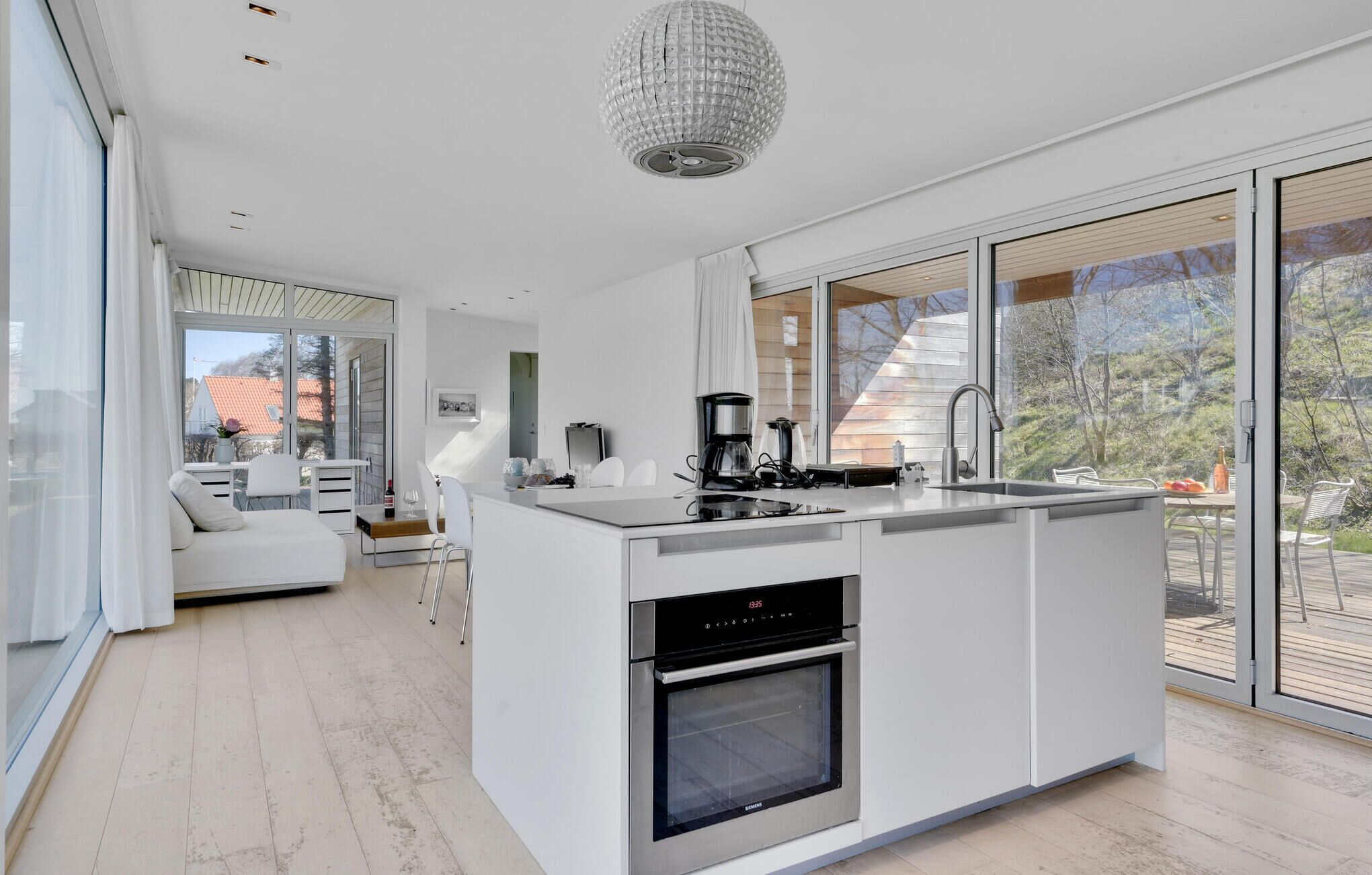 Eine moderne Küche mit einer zentralen Kochinsel, integriertem Backofen und großen Fenstern mit Blick ins Freie.