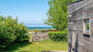 Una casa de madera con vista al mar, una cerca de madera y un jardín cubierto de césped.