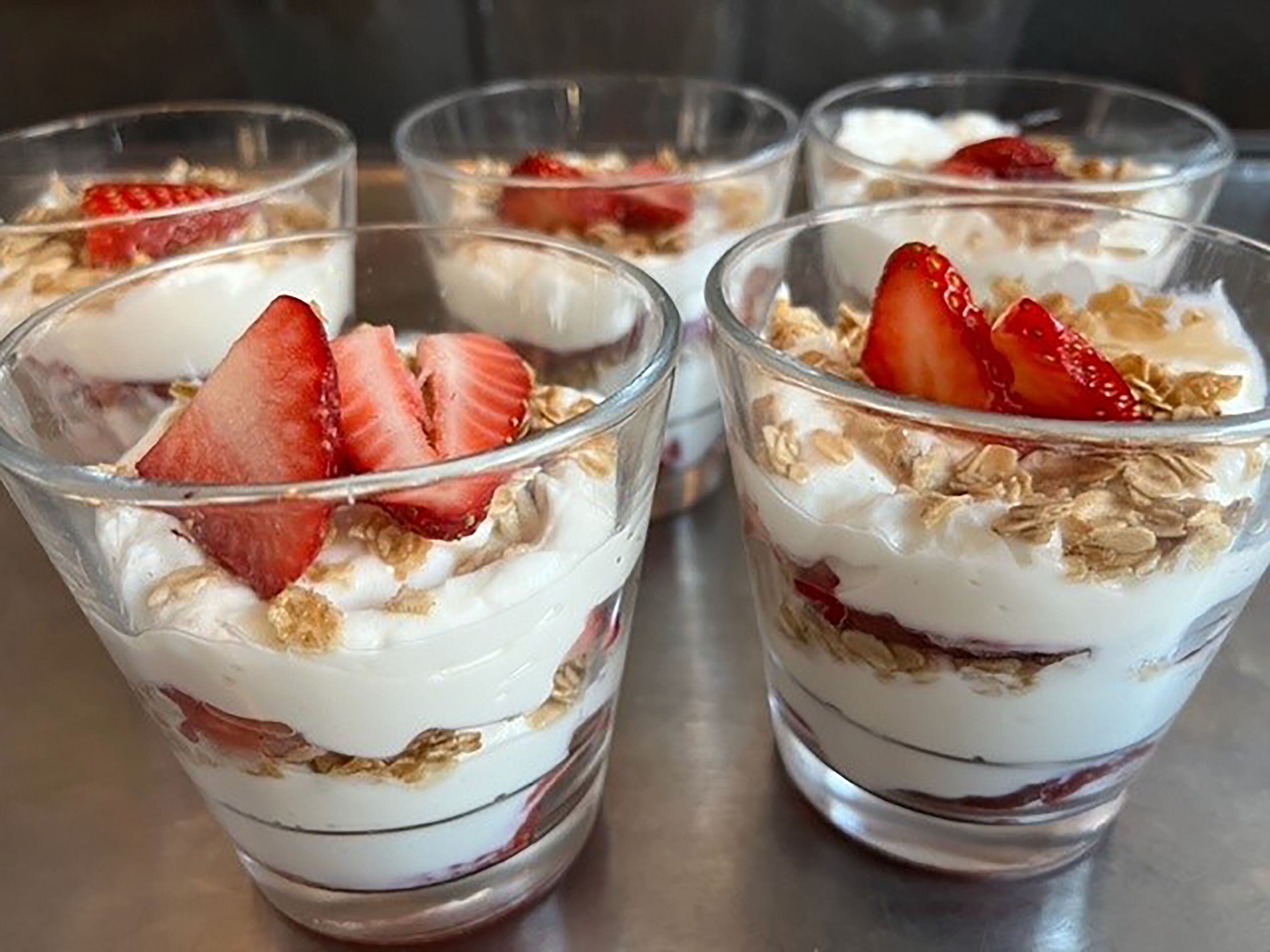 Quatre verrines de dessert en couches, à base de fraises et de granola.