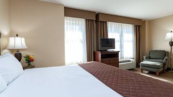 Habitación de hotel con una cama grande, un televisor sobre un soporte de madera, una silla y un escritorio con una lámpara.