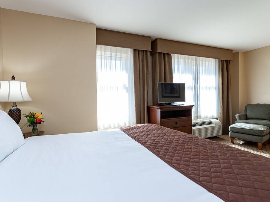 Habitación de hotel con una cama grande, un televisor sobre un soporte de madera, una silla y un escritorio con una lámpara.