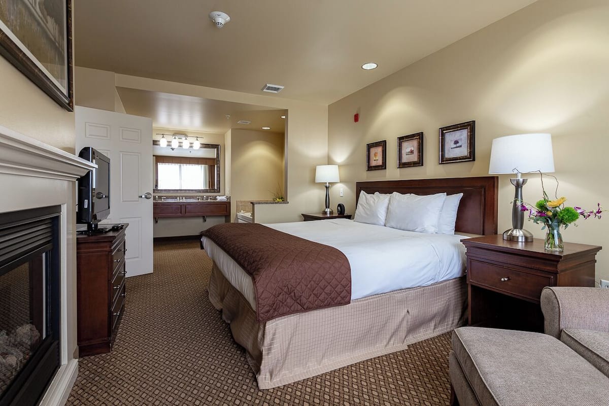 A hotel room with a large bed, a dresser, a TV, and a fireplace.