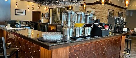 A bar area with a wooden counter, bar stools, and a variety of glassware and bottles.