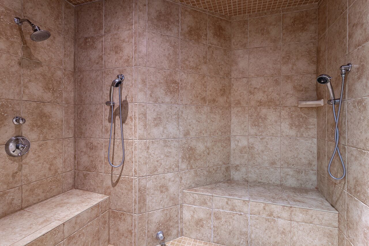 A shower area with beige tiles, a bench, and a handheld showerhead.