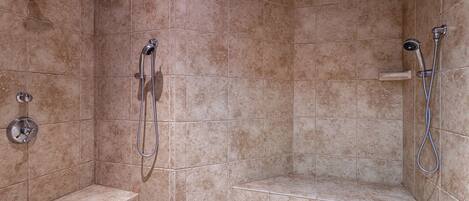Un área de ducha con azulejos color beige, un banco y un cabezal de ducha de mano.