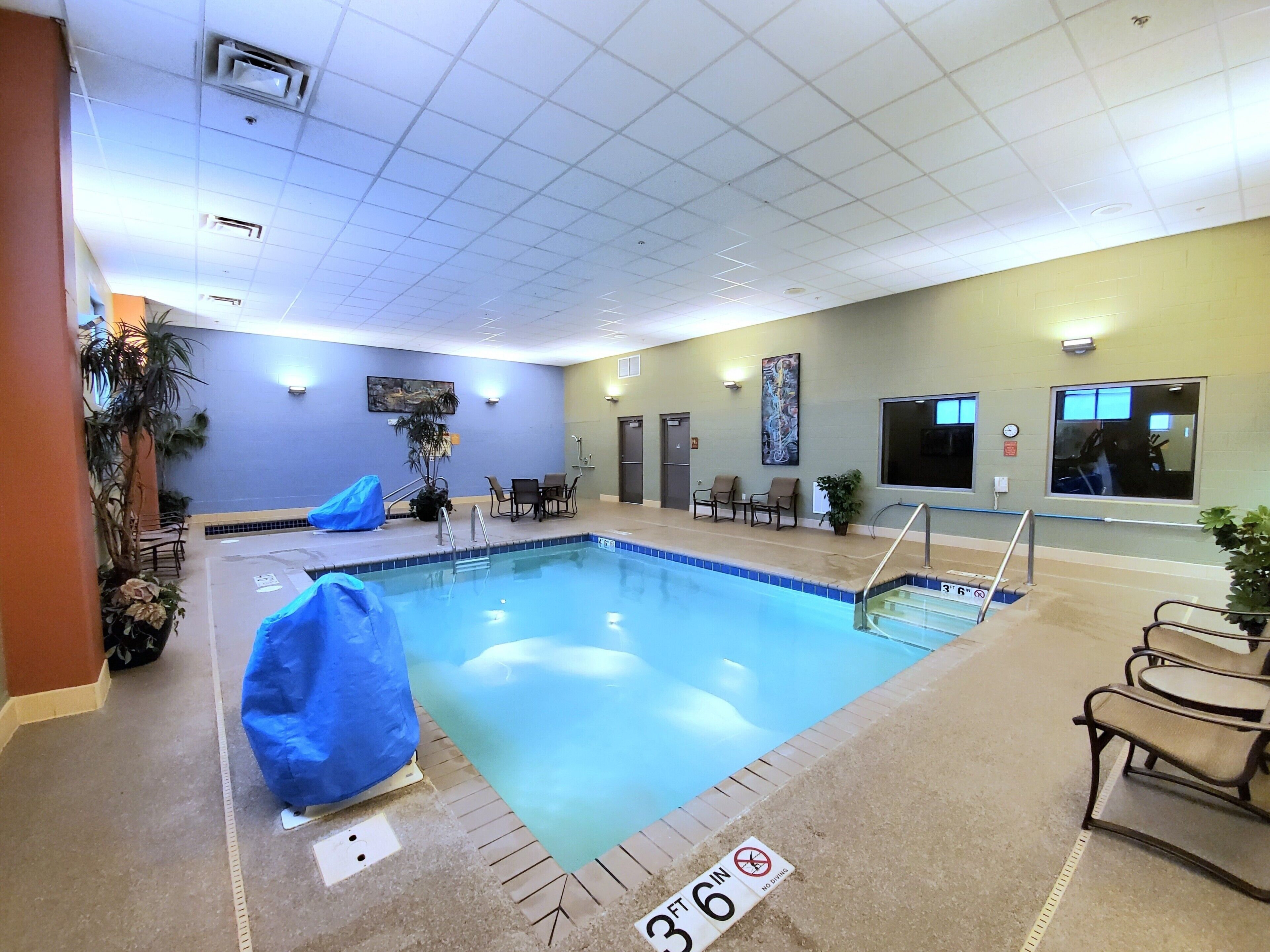 Una piscina interior con indicador de profundidad de 91 centímetros, rodeada de sillones de descanso y un pequeño espacio de estar con una mesa.