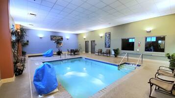 Una piscina interior con indicador de profundidad de 91 centímetros, rodeada de sillones de descanso y un pequeño espacio de estar con una mesa.