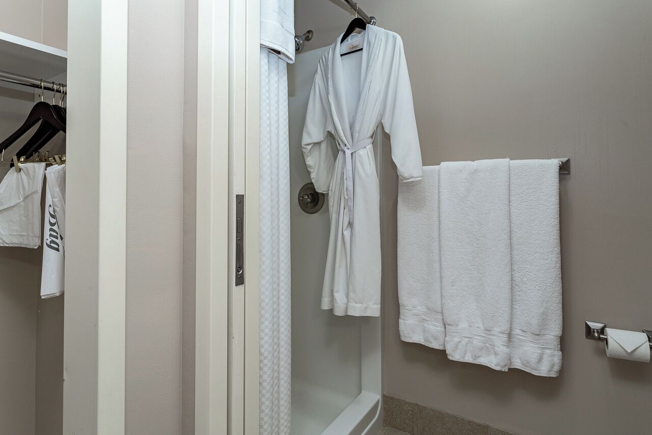 Een badkamer met een glazen douche, een witte badjas hangend aan een rek, en een handdoekrek met een witte handdoek.