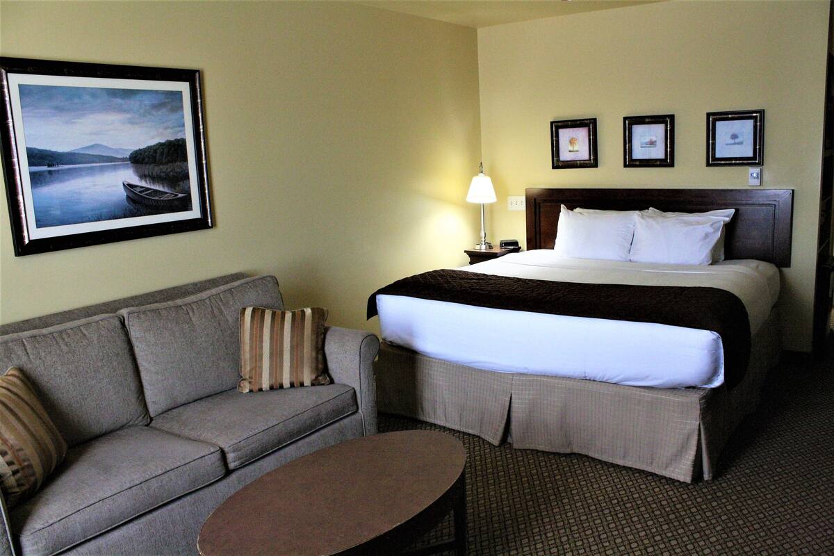 A hotel room with a bed, a sofa, a small table, and a framed picture of a lake.