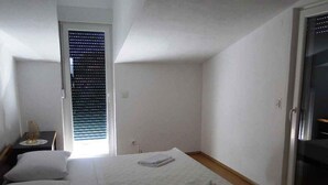 A bedroom with a bed, pillows, a nightstand, and a window with blinds.