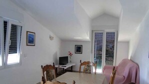 A dining area with a table, chairs, a television, and a sofa with a pink cover.