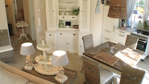 A dining area with wicker chairs, a wooden table, and a white cabinet with glassware.