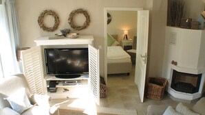A cozy living room with a flat-screen TV, a fireplace, and a bed in the adjacent room.