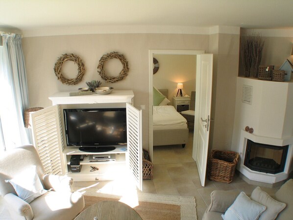 A cozy living room with a flat-screen TV, a fireplace, and a bed in the adjacent room.