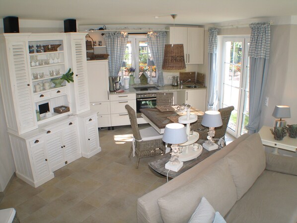 A spacious living room with a beige sofa, a dining table with two lamps, and a kitchen area with a sink and cabinets. - Exclusive apartment with garden and fireplace near the beach (Zingst)