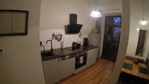 A compact kitchen with a sink, stove, and overhead ventilation hood. There is a dining area with a table and chairs visible through an open doorway. - 3-room guest apartment close to the center, suitable for 1 - 4 persons (Leipzig)