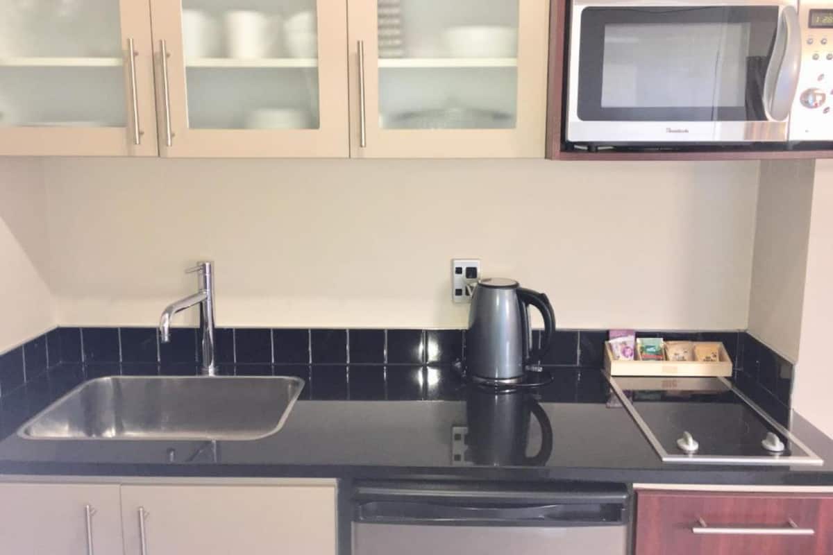 Una cocina con un lavamanos, estufa, hervidor y microondas.