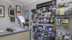 A reception area with a wall display of travel brochures and a sign indicating visitor information. - Kauri Motel (Christchurch)
