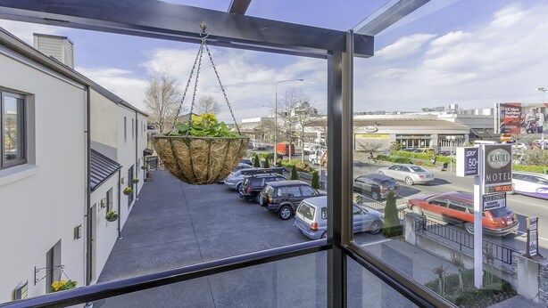 A view from a window overlooking a parking lot with a hanging basket of plants, a motel sign, and a clear sky. - Kauri Motel (Christchurch)
