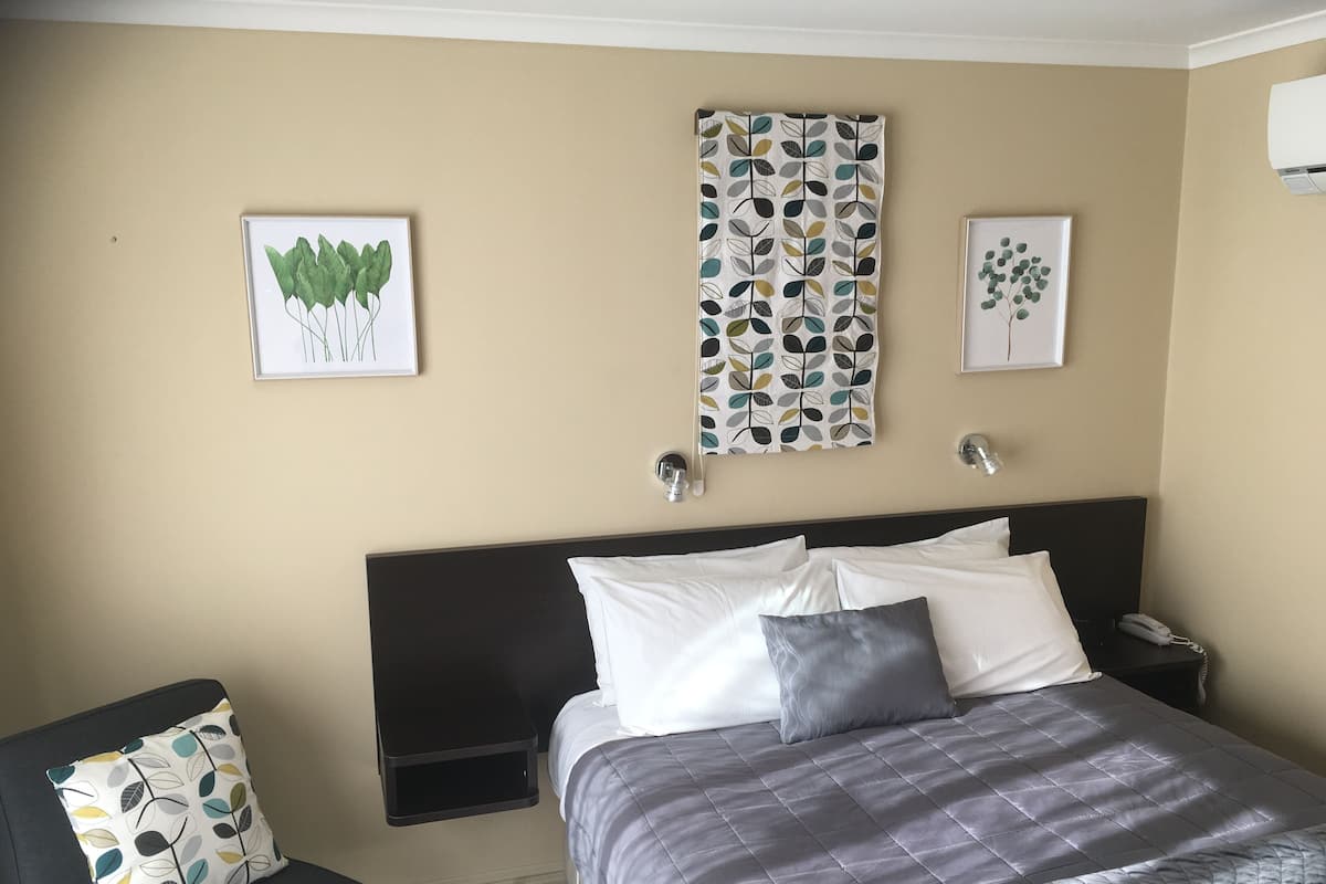 Habitación de hotel con cama, mesitas de noche, una silla y una obra de arte en la pared.