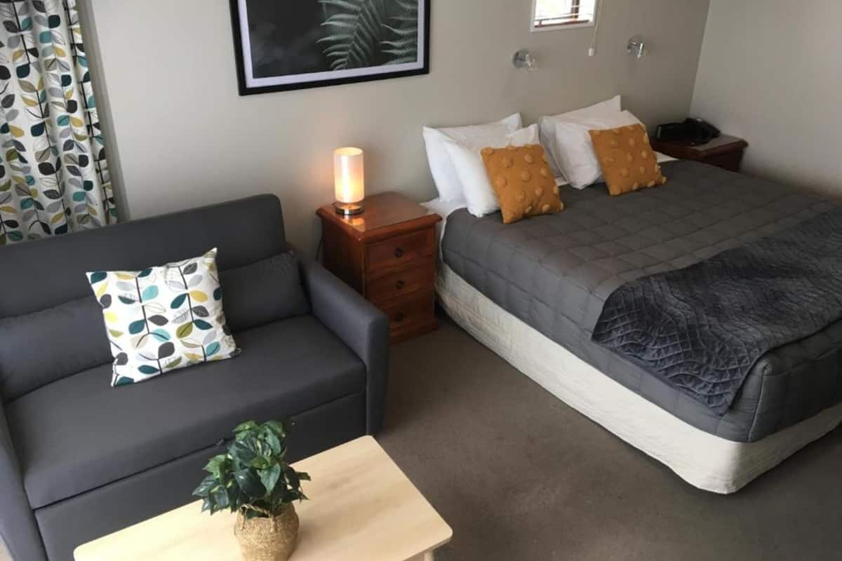 Un dormitorio con cama, sofá, mesita de noche, lámpara y un cuadro en la pared.