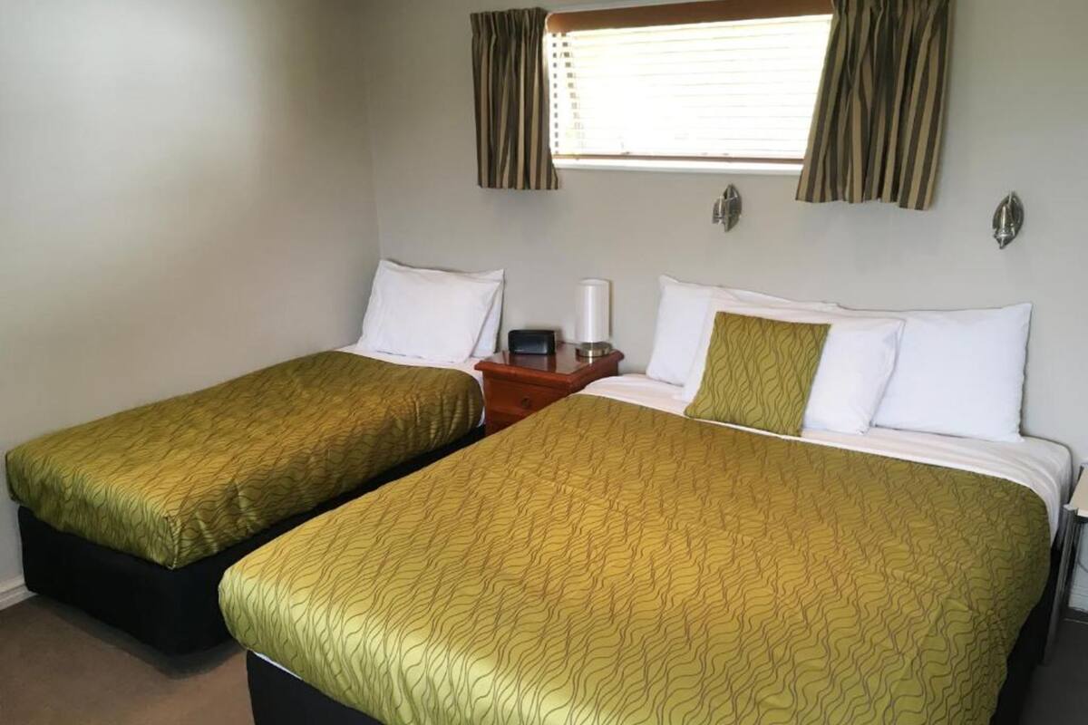 Habitación de hotel con dos camas individuales, cada una con una colcha verde estampada, almohadas blancas y una mesita de noche con lámpara.
