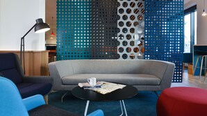 Un espace de détente moderne avec un canapé gris, des fauteuils bleus, une table basse noire et un pouf rouge.