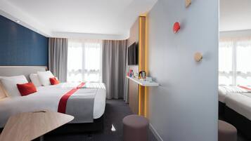 Ett hotellrum med en säng, ett skrivbord, en stol, en tv och en hylla som är monterad på väggen.