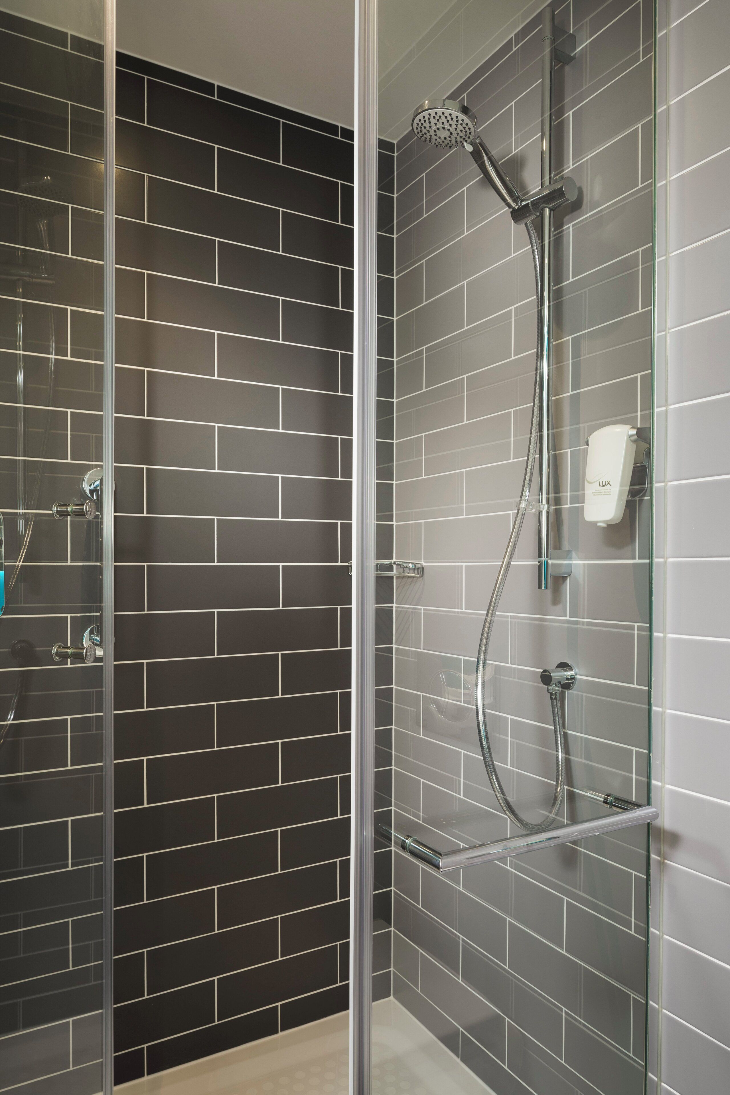 A modern shower with a glass door, a handheld showerhead, and a handheld shower attachment.