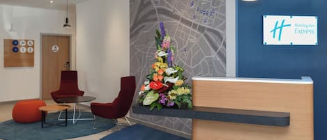 A hotel reception area with a wooden reception desk, red chairs, a map on the wall, and a sign for Holiday Inn Express.