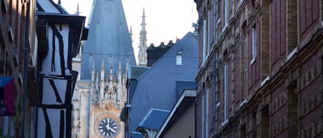 Una calle estrecha con edificios históricos, una imponente torre del reloj y la aguja de una iglesia.