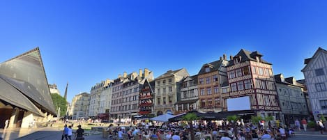Uma área movimentada de café ao ar livre, com arquitetura europeia tradicional, cercada por uma multidão de pessoas.