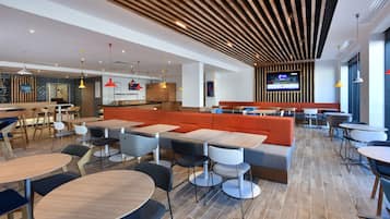 Un restaurante moderno con mesas altas, cabinas y una pantalla de televisión en la pared.