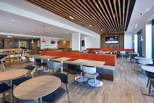 Um restaurante moderno com mesas altas, cabines e uma tela de TV na parede.