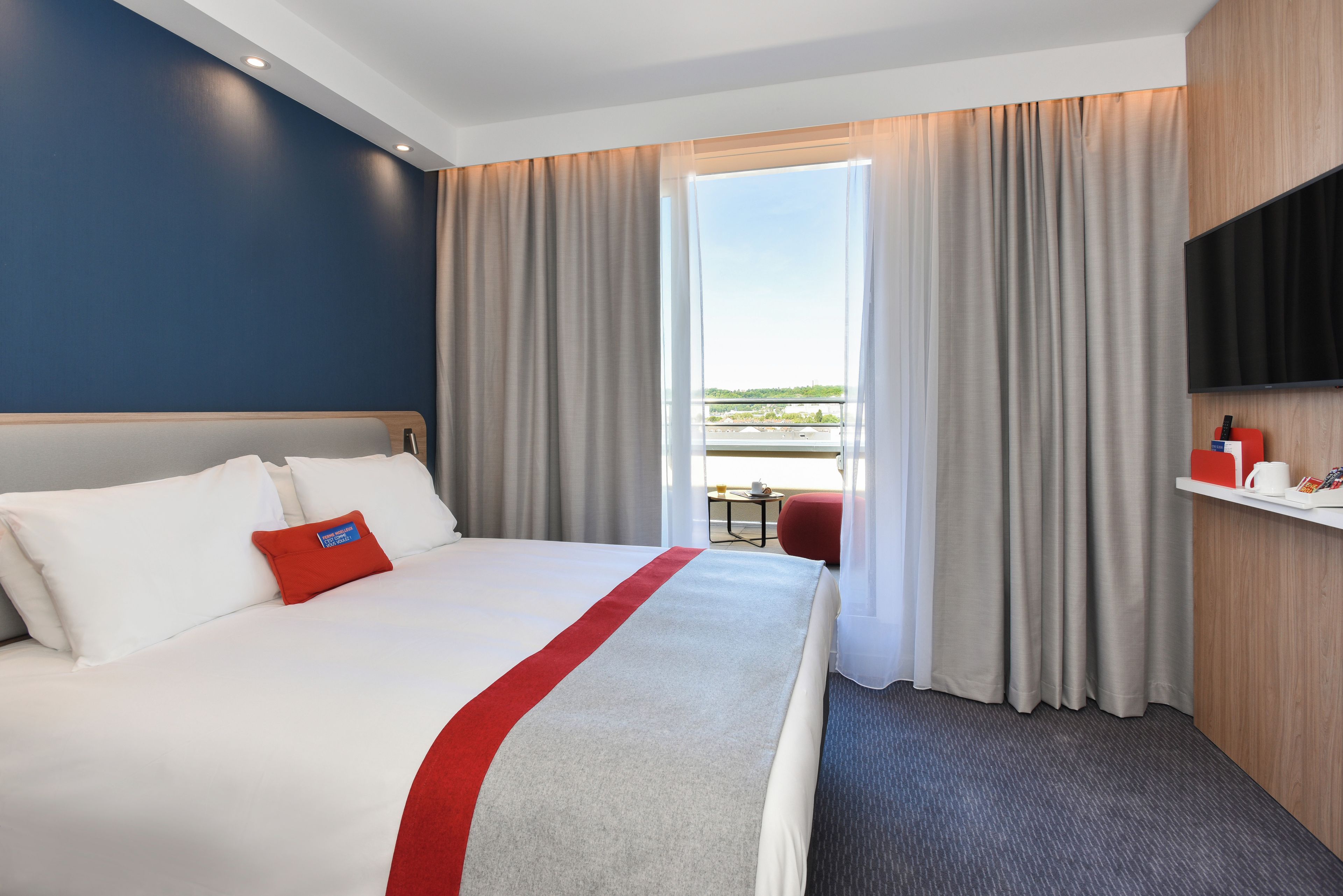 Habitación de hotel con una cama grande, un televisor, una mesita con una taza y vistas a la ciudad.