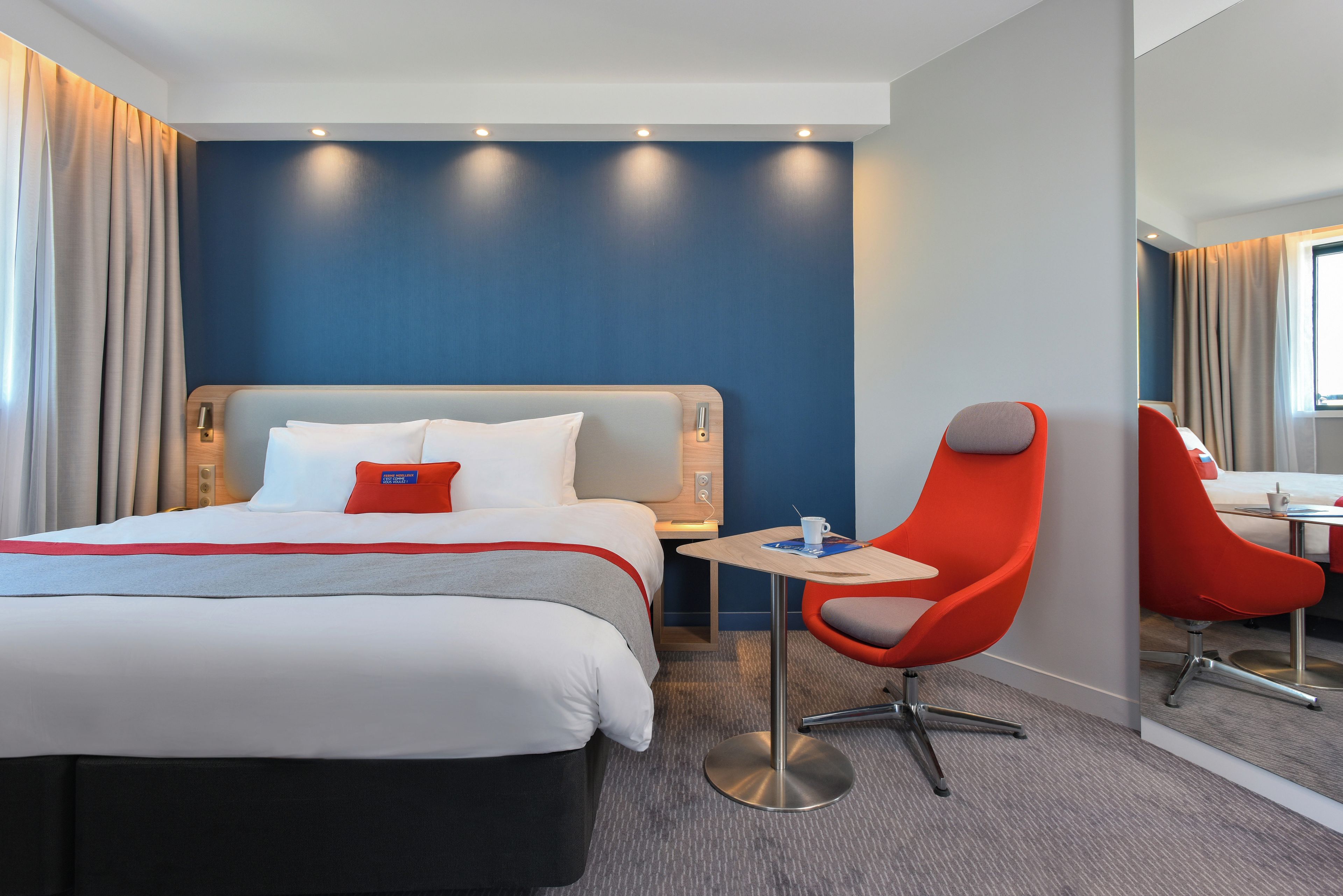 A hotel room with a bed, a desk, a chair, and a mirror.