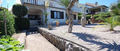 A two-story building with a stone pathway leading to the entrance, surrounded by potted plants and a palm tree.
