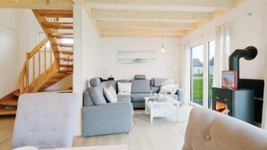 A cozy living room with a grey sofa, a white coffee table, and a fireplace. A wooden staircase is visible on the left.