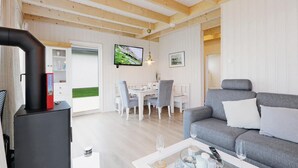 A cozy living room with a grey sofa, a dining area with white chairs, and a TV mounted on the wall.