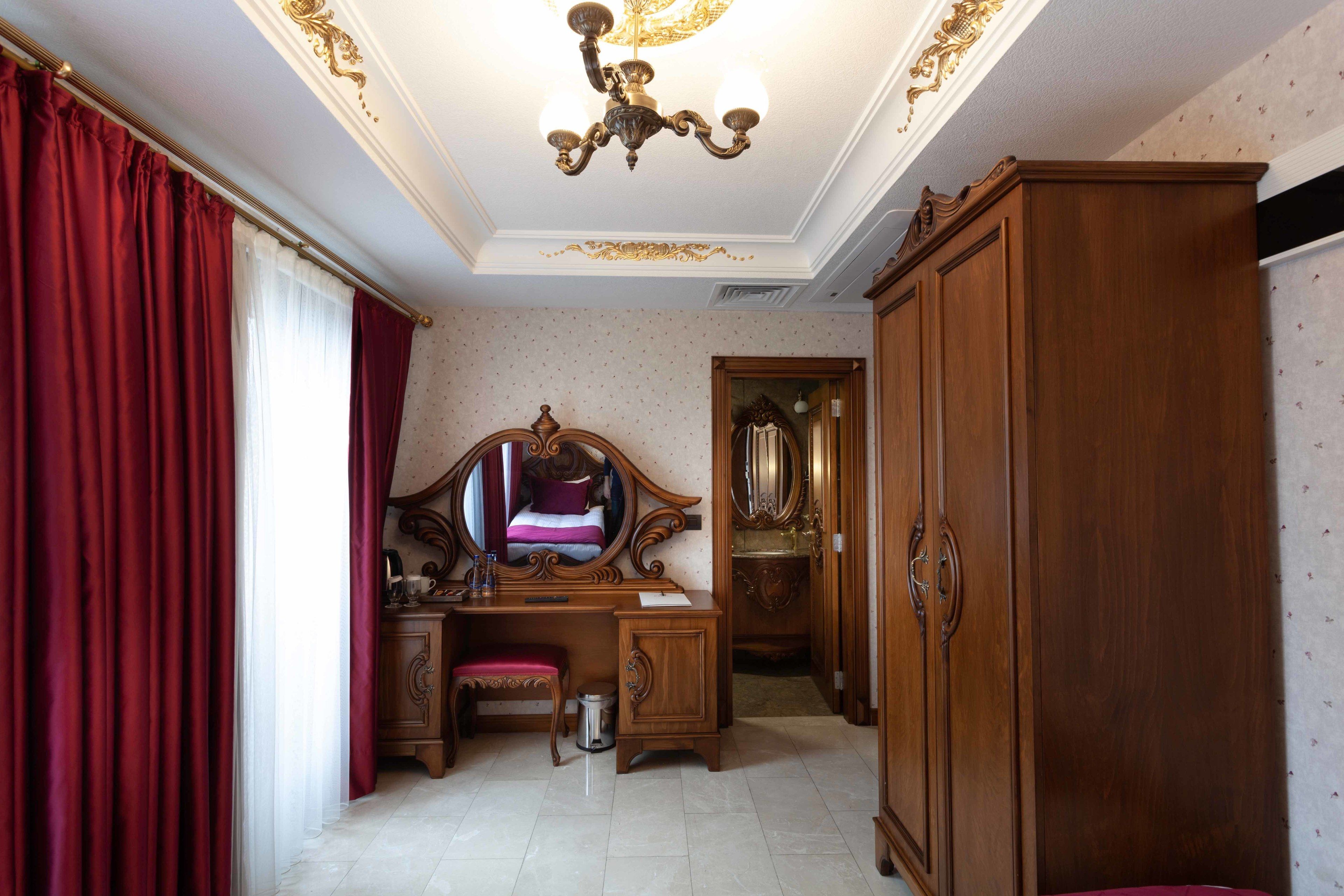 A room with a wooden desk, a mirror, a wardrobe, and a chandelier.