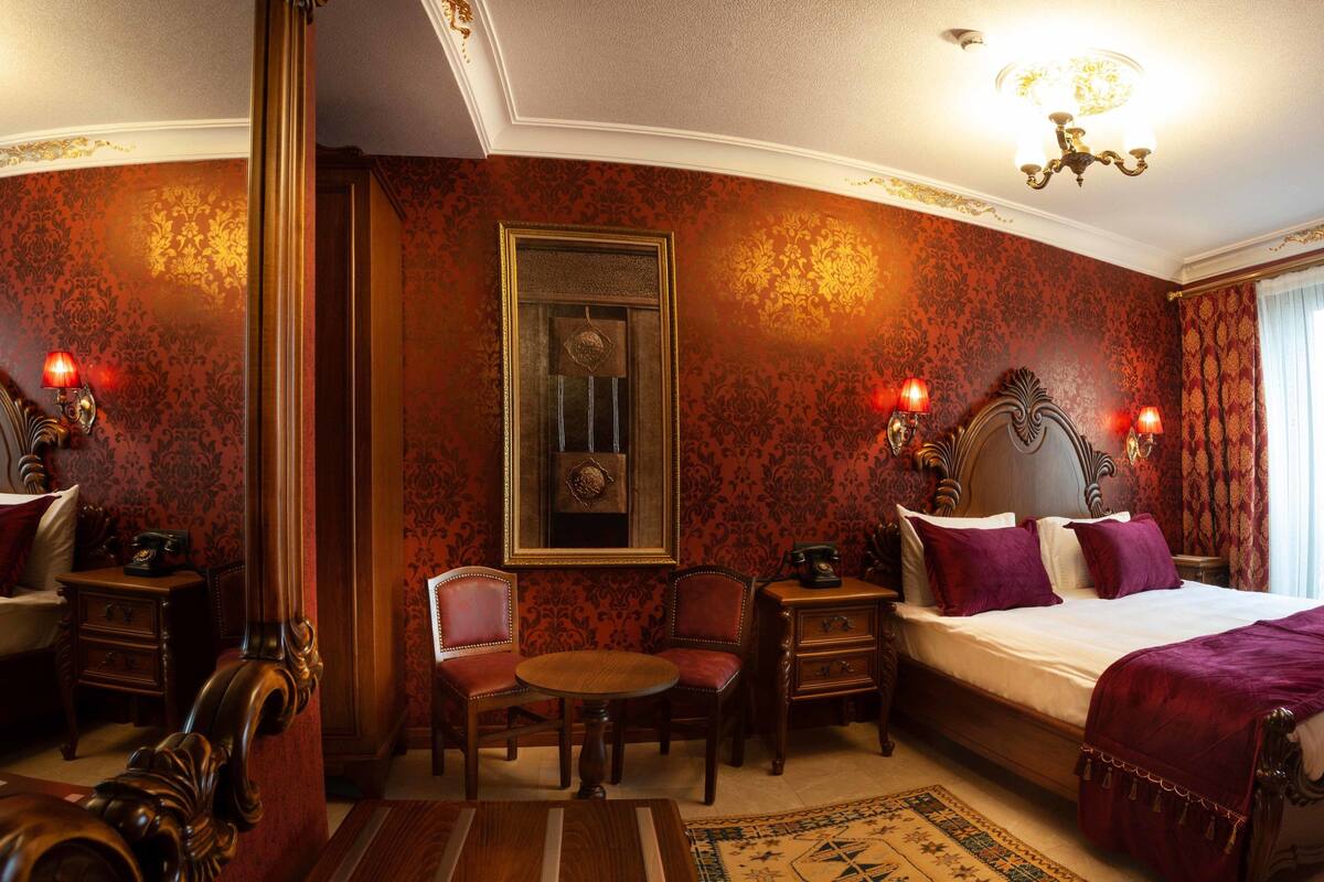 A hotel room with a large bed, two bedside tables, a chair, a small table, and a chandelier.