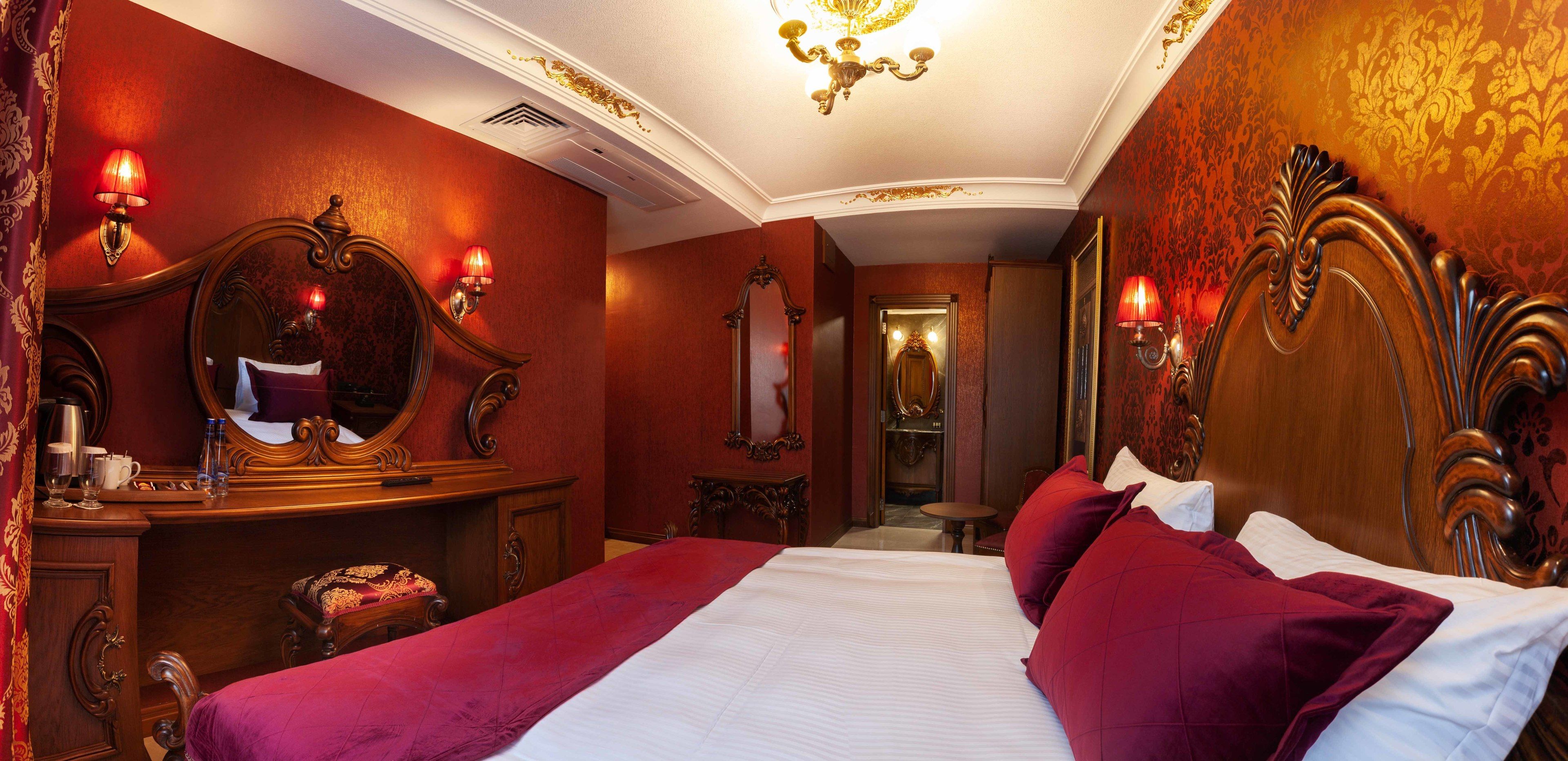 A hotel room with a large bed, a vanity with a mirror, and two wall sconces.