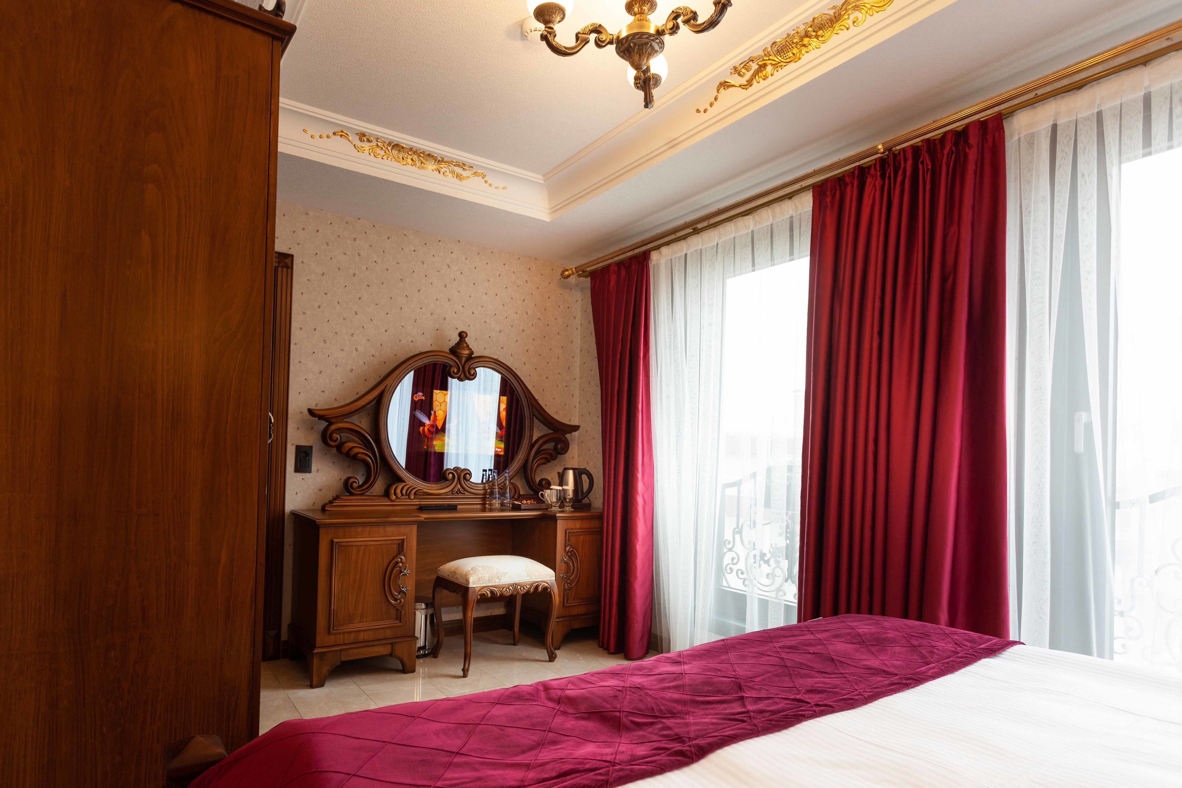 A bedroom with a large bed, a wooden dresser with a mirror, and a window with red curtains.