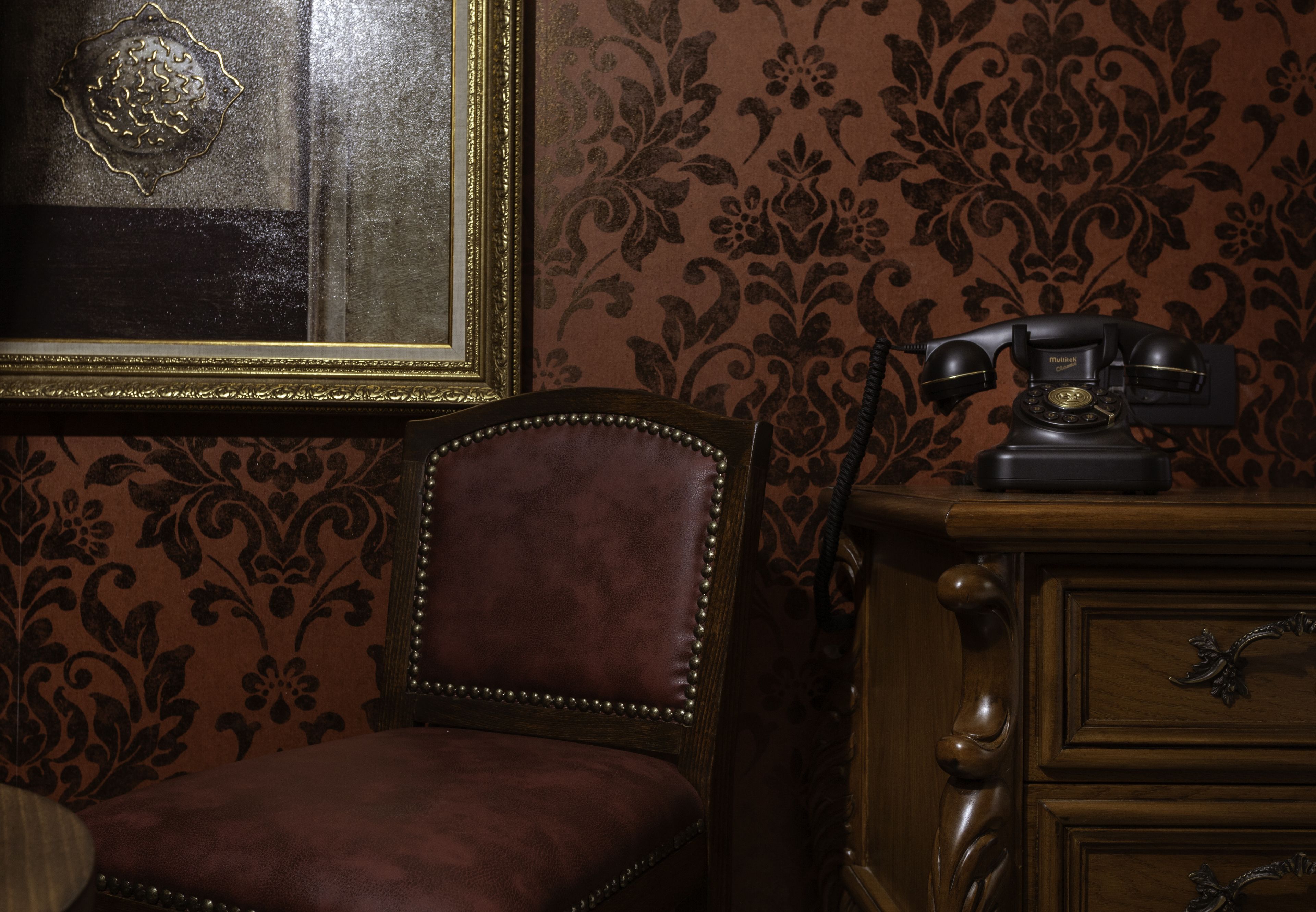 A vintage room with a leather chair, a wooden dresser, and a patterned wallpaper.