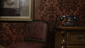 A vintage room with a leather chair, a wooden dresser, and a patterned wallpaper.