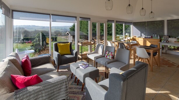 A spacious living area with a large window overlooking a scenic landscape, a dining area with a kitchen in the background, and comfortable seating arrangements. - My Way Guest House (Durham)